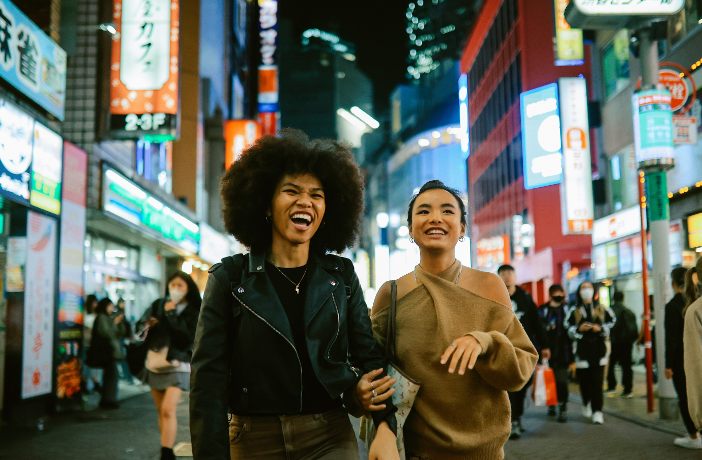 two female friends smile and laugh as they stroll Tokyo, Japan, at night after looking up what to do in an earthquake while traveling