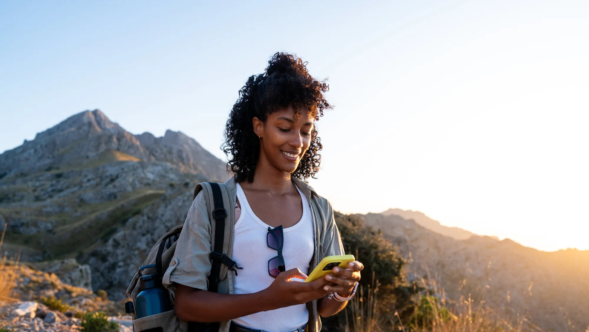 a hiker uses her smartphone on a mountain trail to look up the difference between a travel alert and advisory
