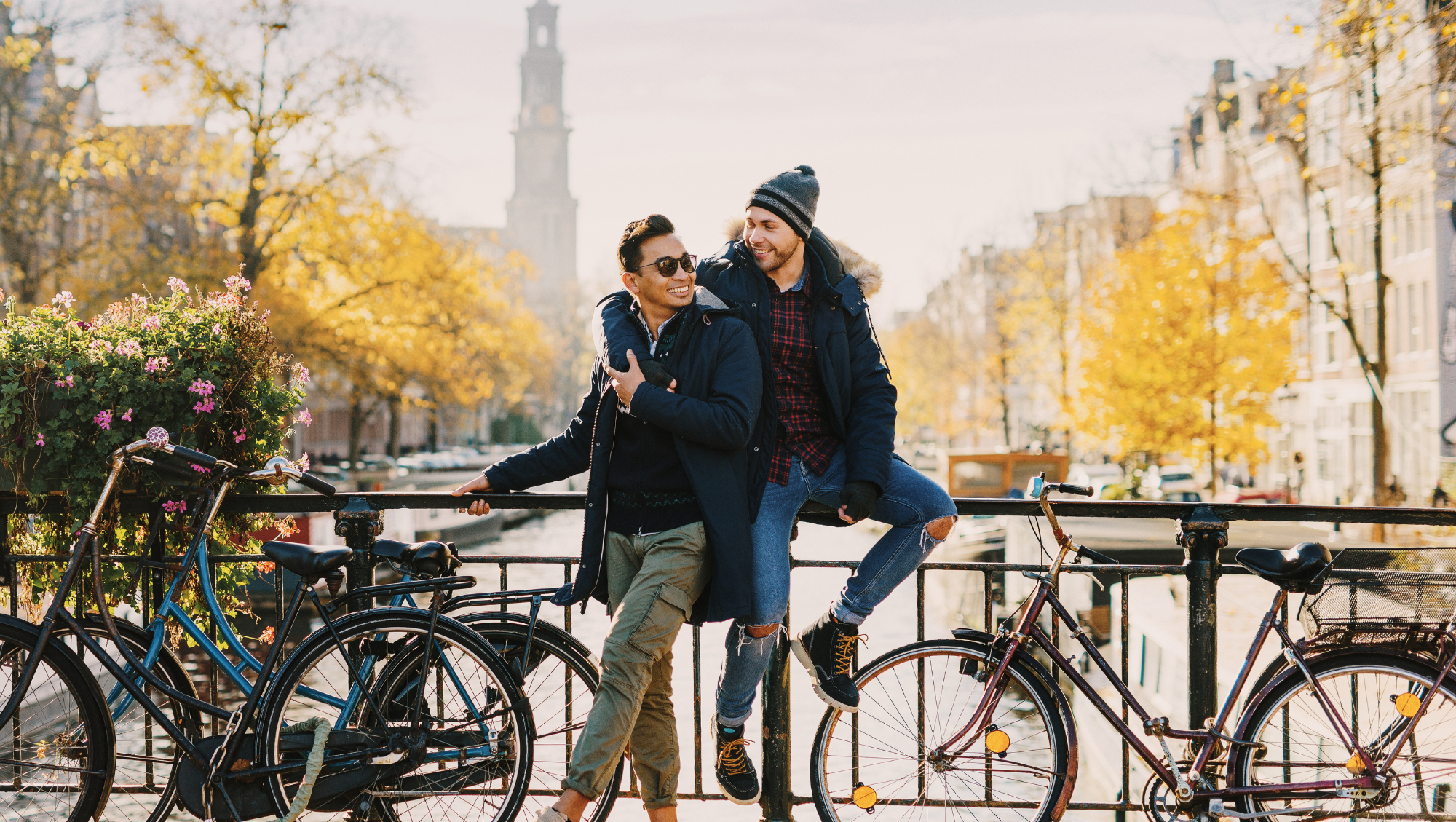 two male partners pose for a picture in a city in autumn by bikes after researching LGBTQ travel tips