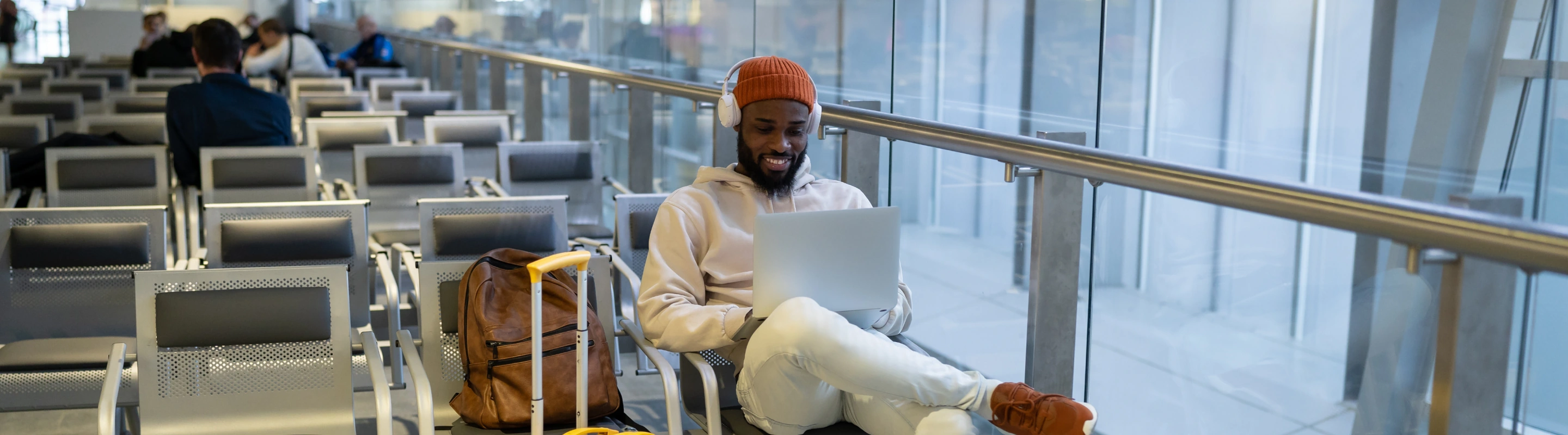 Young man with travel insurance for digital nomads using his laptop in the airport while sitting at the gate