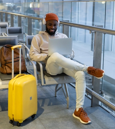 Young man with travel insurance for digital nomads using his laptop in the airport while sitting at the gate