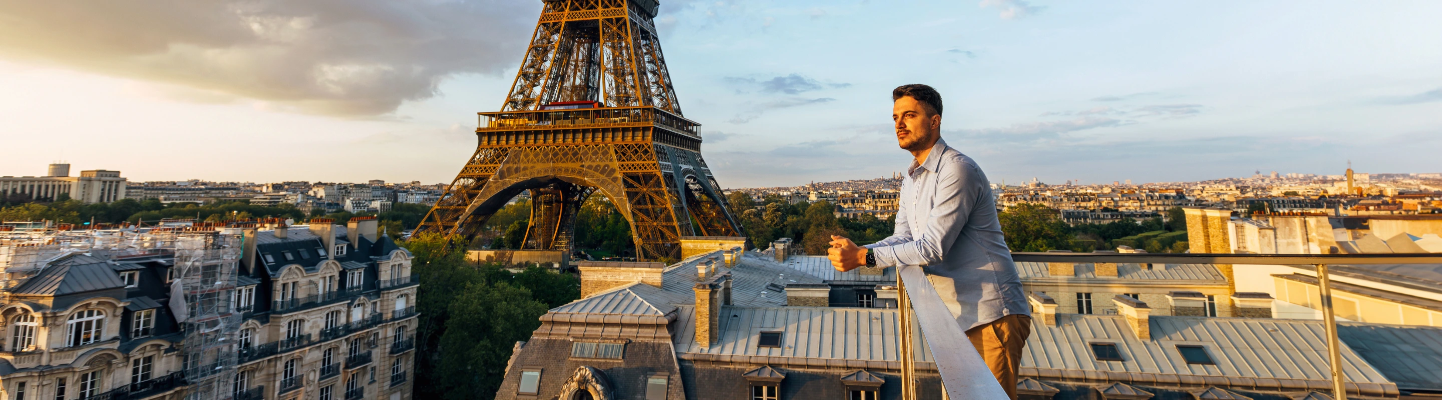 a young man with solo travel insurance overlooks the Eiffel Tower from a balcony at sunset 