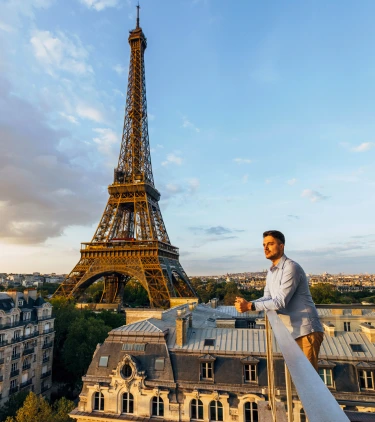 a young man with solo travel insurance overlooks the Eiffel Tower from a balcony at sunset 