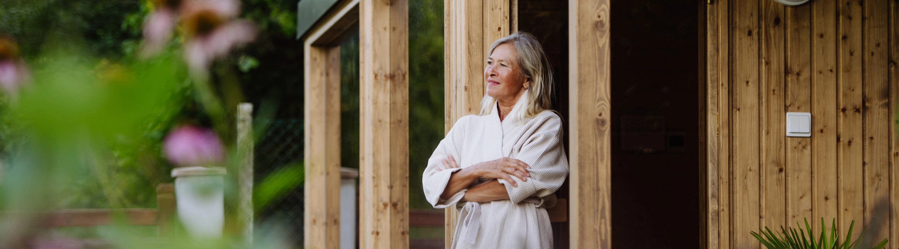 an older woman with travel insurance for wellness retreats stands outside a wooden spa in her robe