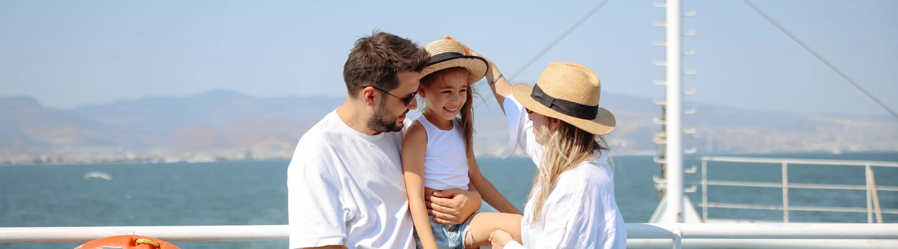 parents with cruise travel insurance hold their daughter and put a hat on her head on a ship