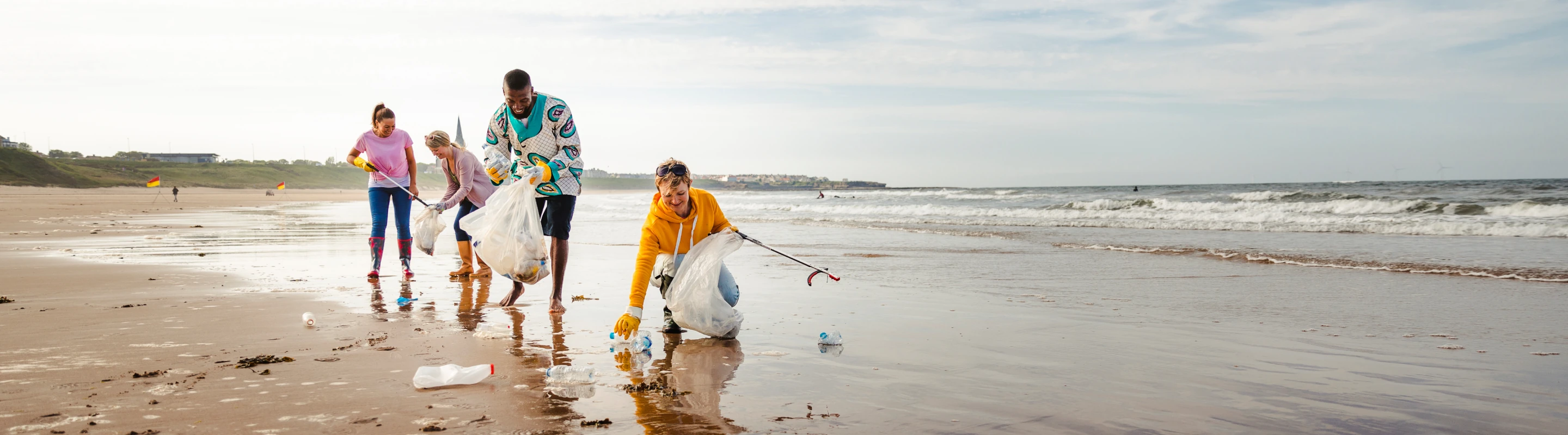 Four adults with volunteer travel insurance holding trash bags and picking up trash on the beach