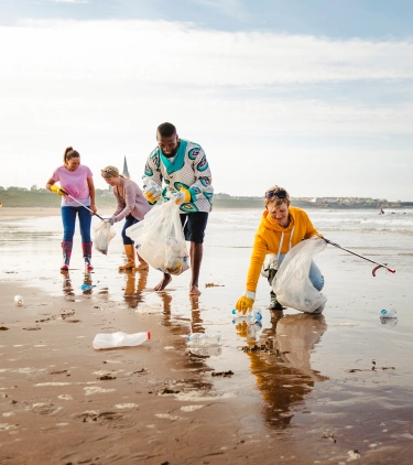 Four adults with volunteer travel insurance holding trash bags and picking up trash on the beach