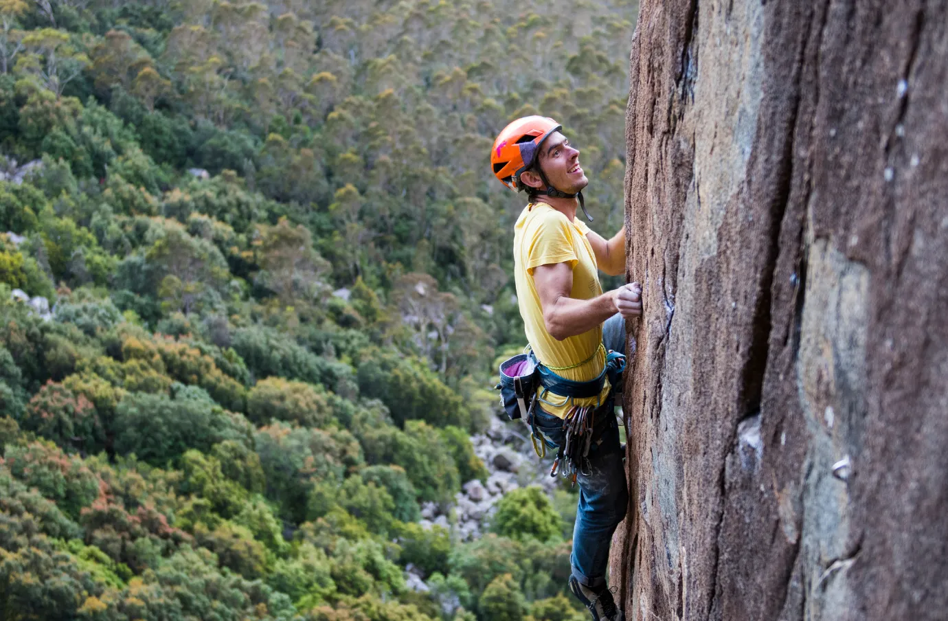 a male climber with adventure travel insurance ascends a mountain cliff with safety gear