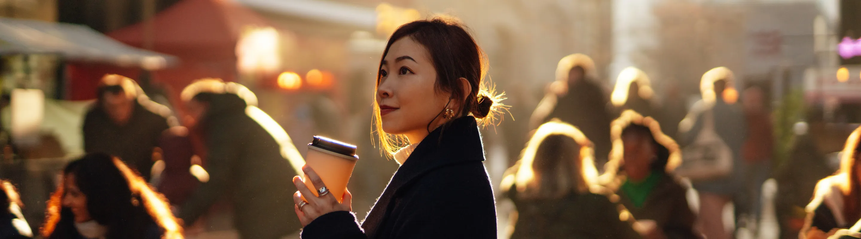 a solo female traveler holds a coffee and explores a local market, insured with travel insurance for city trips