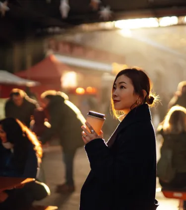 a solo female traveler holds a coffee and explores a local market, insured with travel insurance for city trips