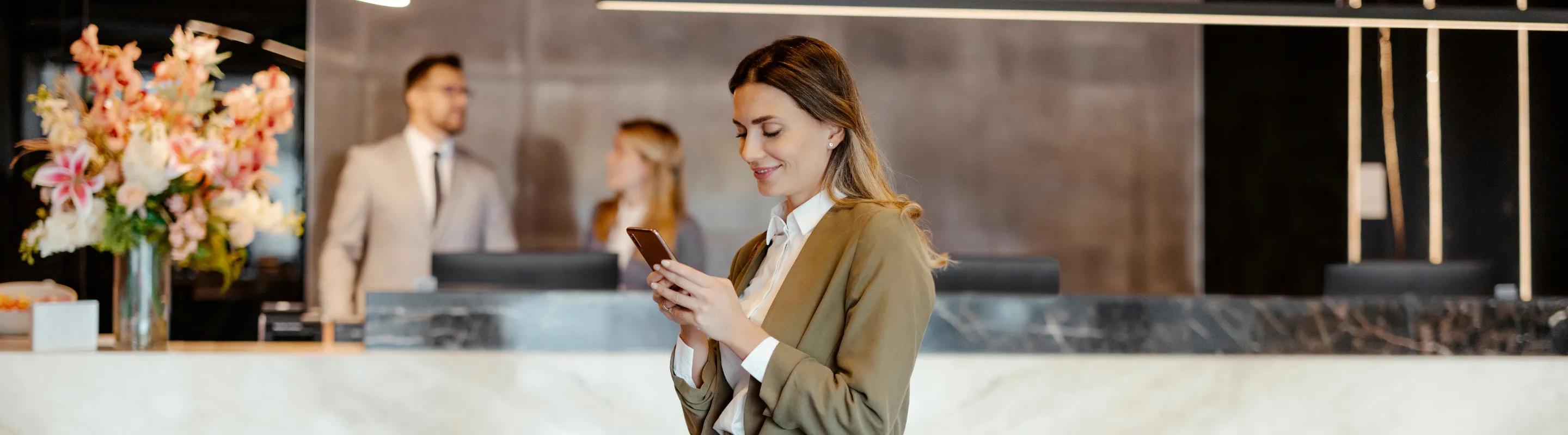 a female traveler looks at her phone as she checks into a hotel, insured with business travel insurance 