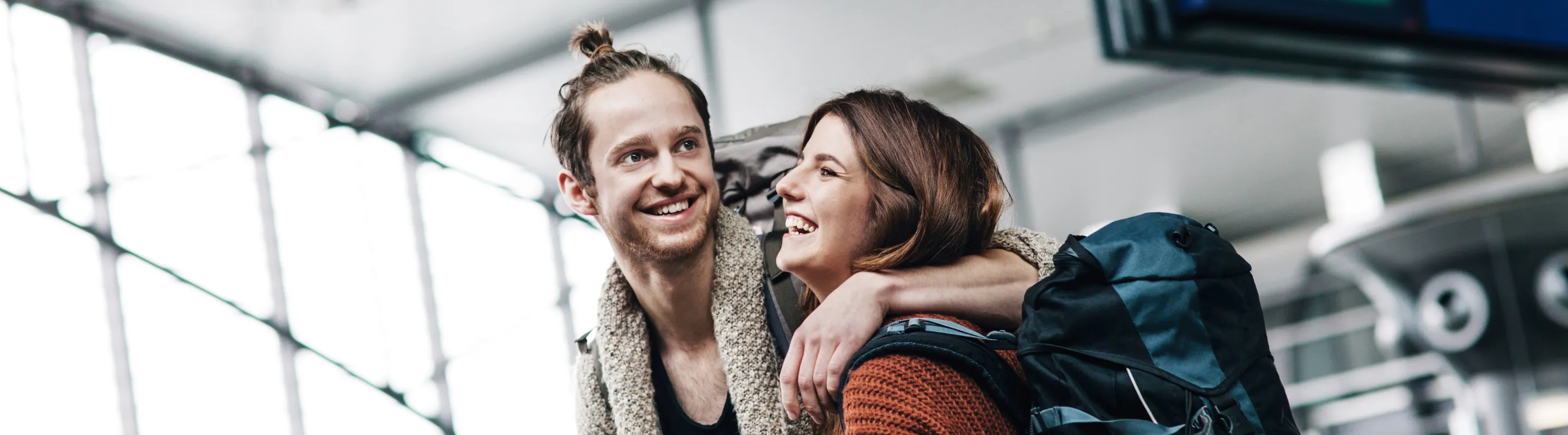 a young couple smiles and embraces in an airport terminal, insured with backpacker travel insurance 