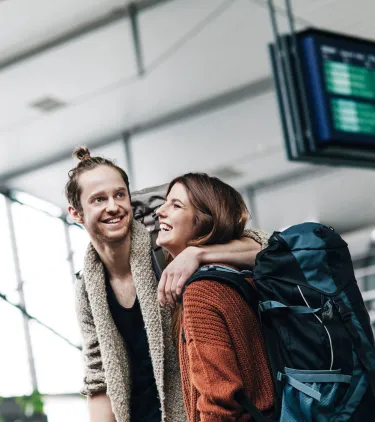 a young couple smiles and embraces in an airport terminal, insured with backpacker travel insurance 