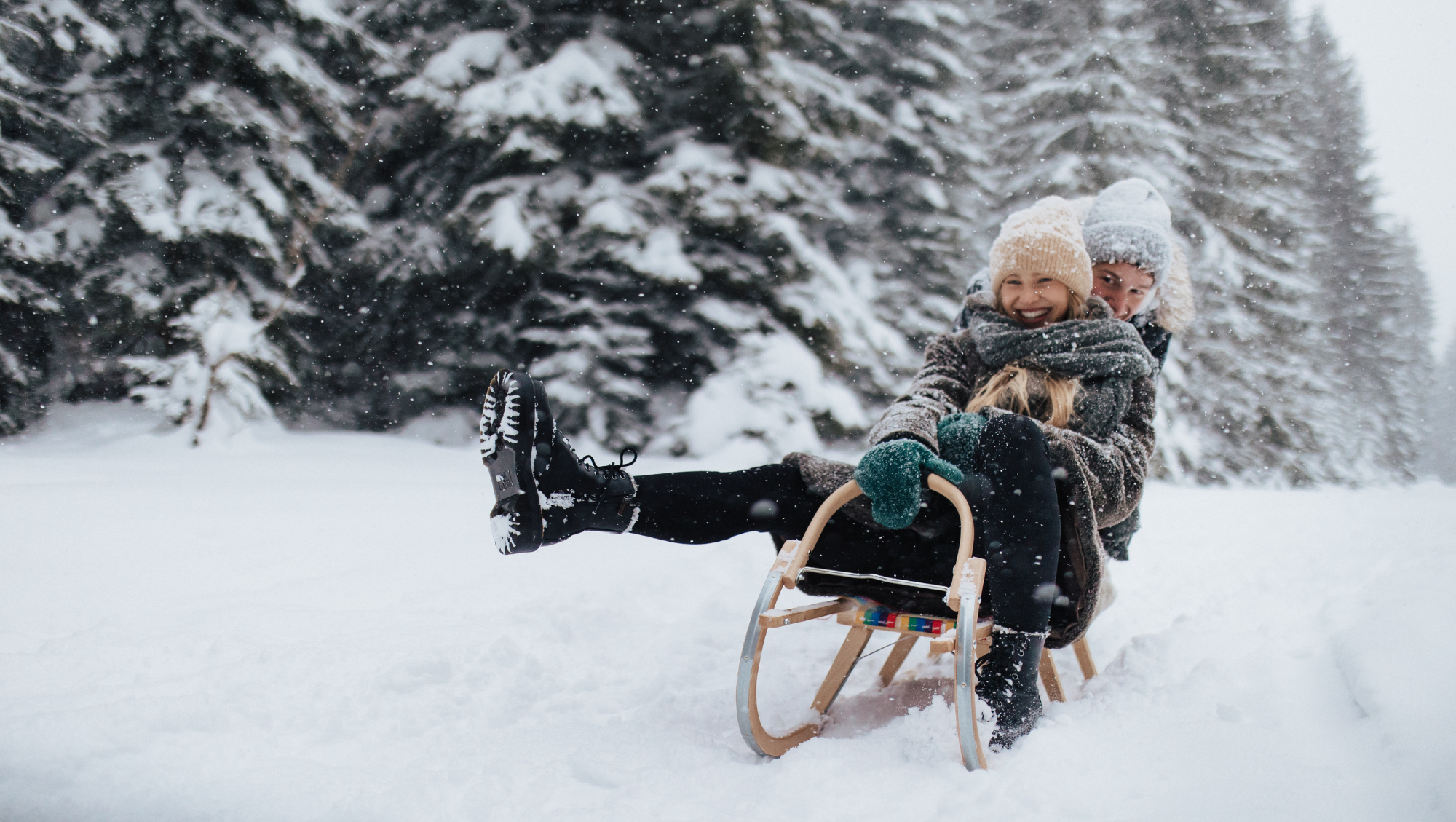two children laugh as they sled outdoors, after their parents looked up, "Does travel insurance cover snowstorms?"