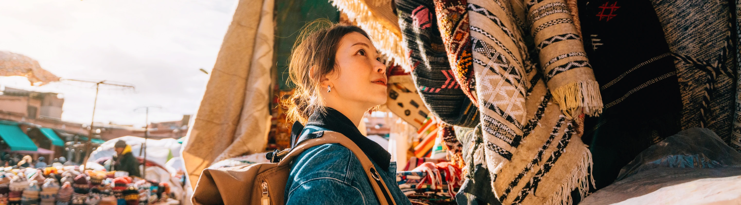 a woman with solo travel insurance browses rugs at a local market on vacation