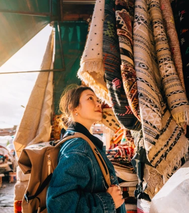 a woman with solo travel insurance browses rugs at a local market on vacation