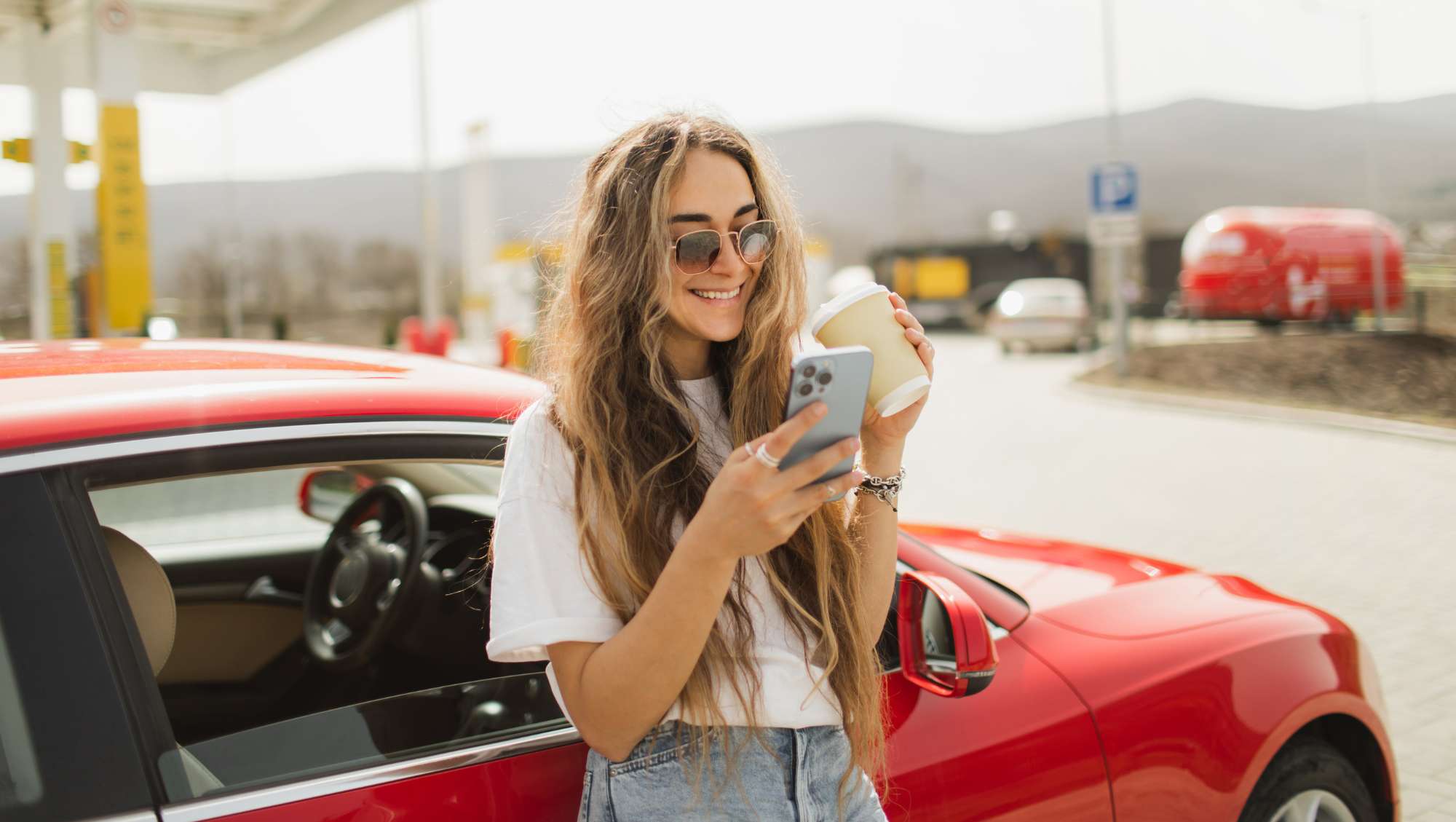 a young woman checks the travel app on her phone at a gas station