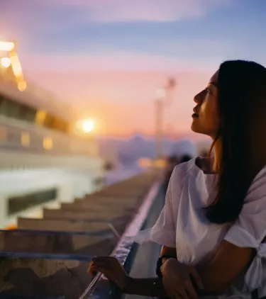 a young woman admires a twinkling cruise ship at sunset, insured with cruise travel insurance 