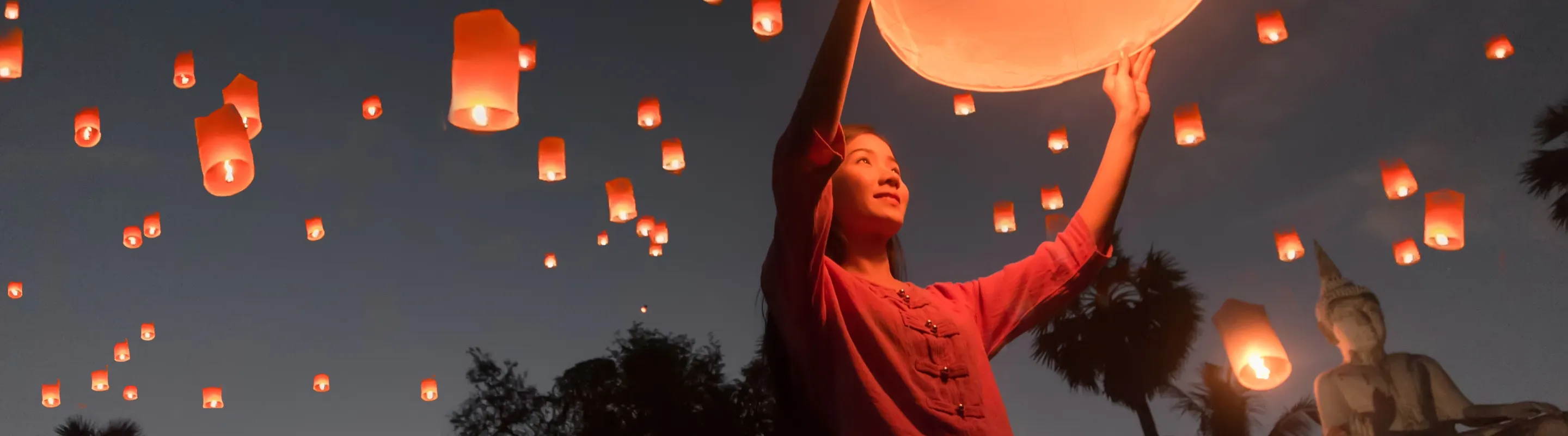 a woman launches a floating lantern into the sky at a night festival, insured with pilgrimage travel insurance 