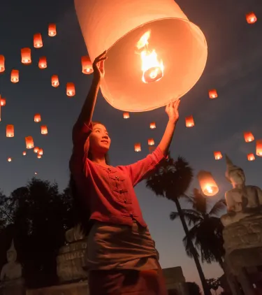 a woman launches a floating lantern into the sky at a night festival, insured with pilgrimage travel insurance 