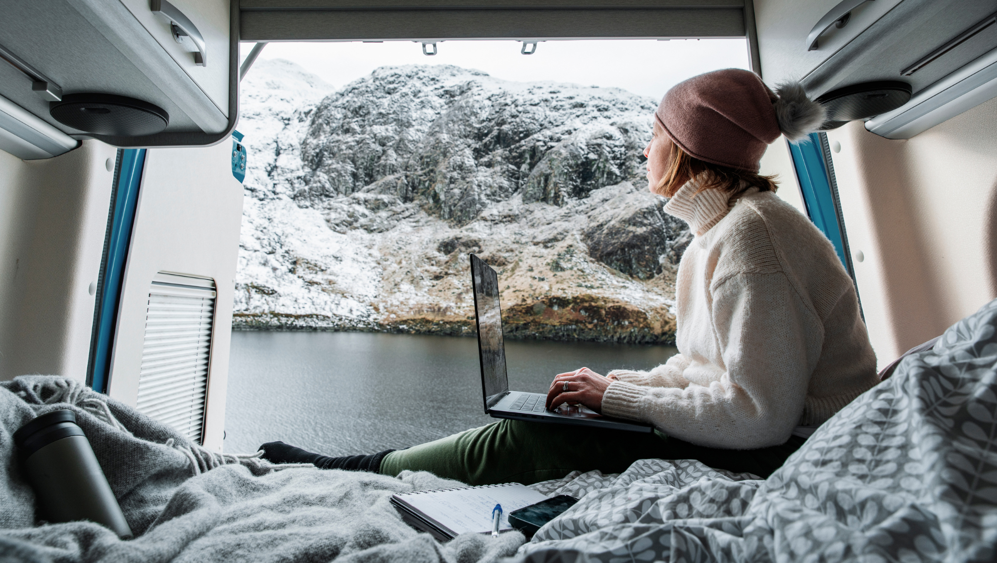 a woman sits on her laptop in her van by a mountain, looking up "How much is travel insurance?"