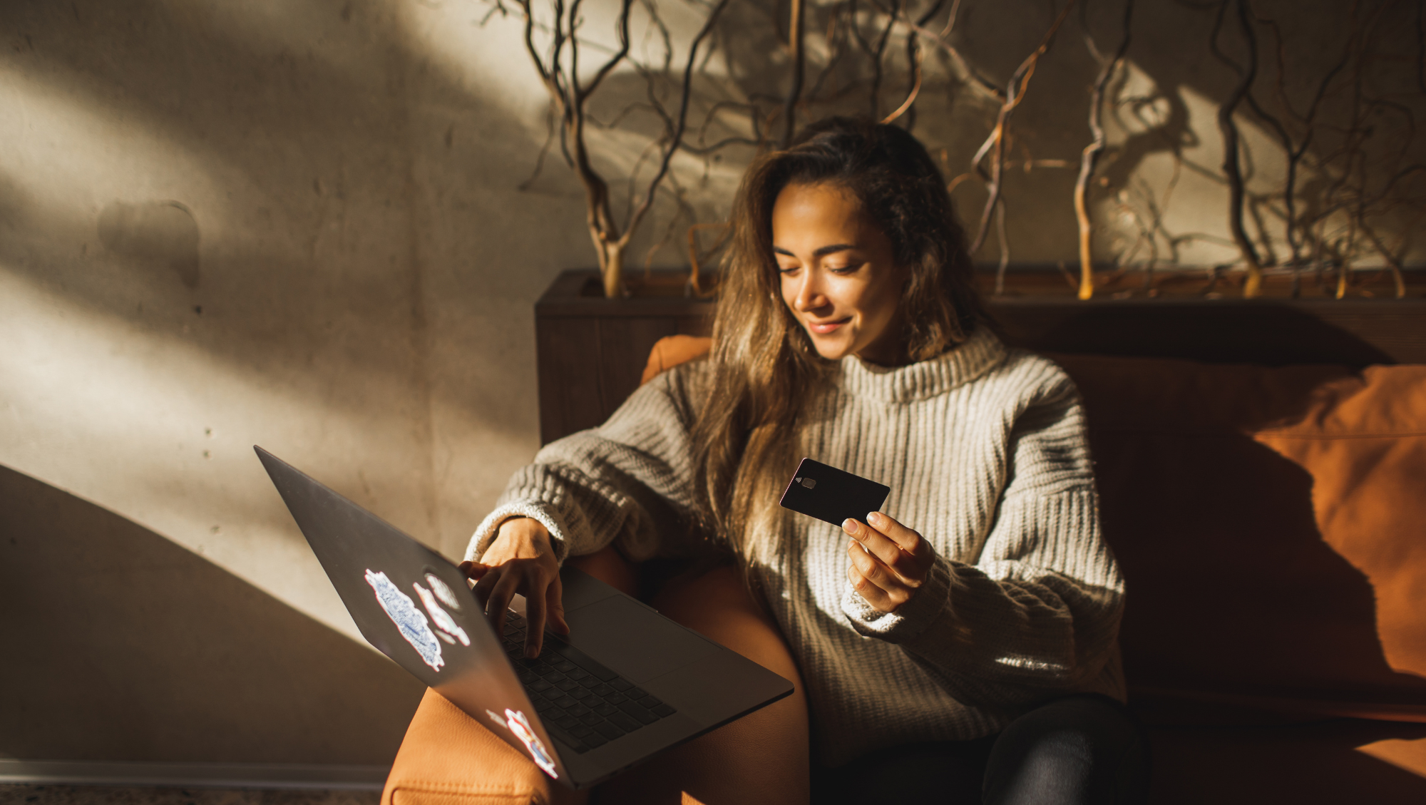 young woman at home holding a credit card while using her laptop to search "How much is travel insurance?"