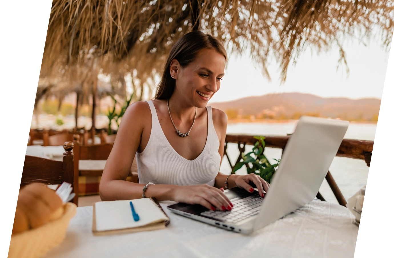 Woman with travel insurance for digital nomads using her laptop by the ocean and sitting under a thatched roof