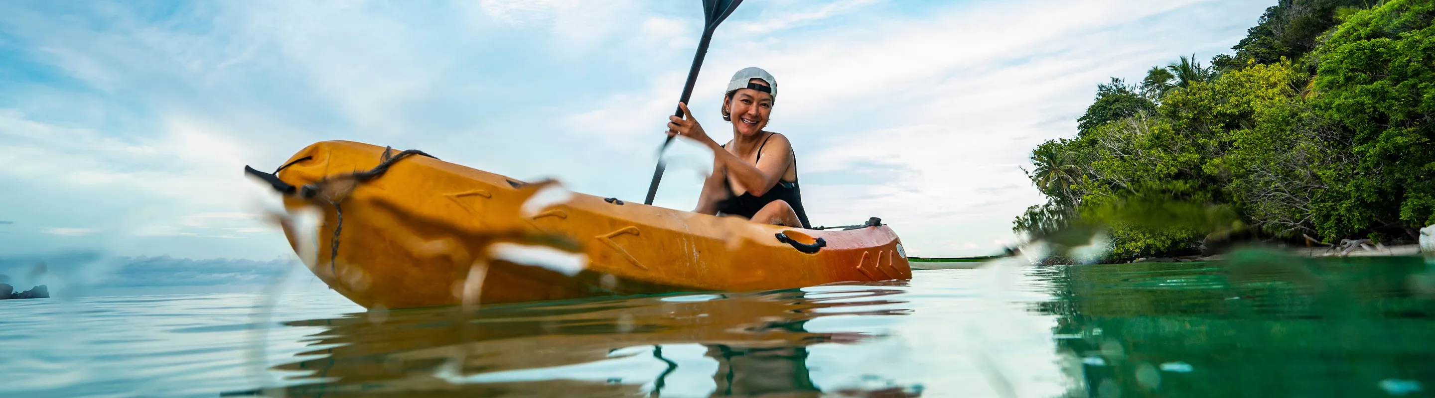 a woman with adventure travel insurance paddles her kayak through a crystal-clear lagoon