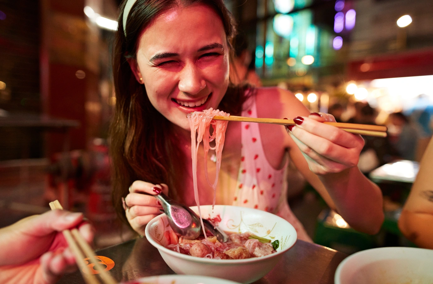 a woman slurps ramen at a night market with travel insurance for culinary trips