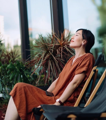 a middle-aged woman with travel insurance for wellness retreats relaxes in a garden lounge chair in an orange dress