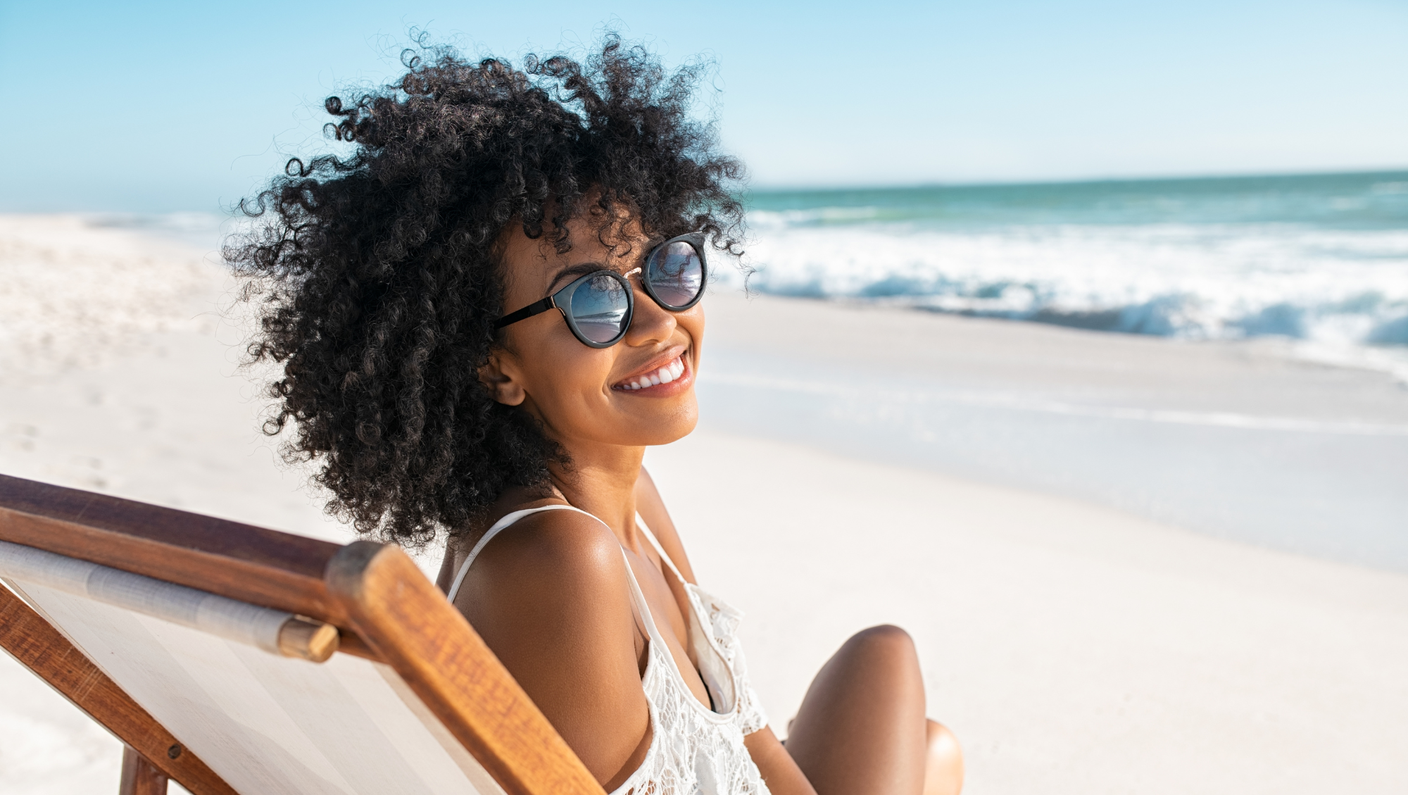 a woman relaxes on a beach chair wearing sunglasses, looking relaxed after researching hurricane safety tips
