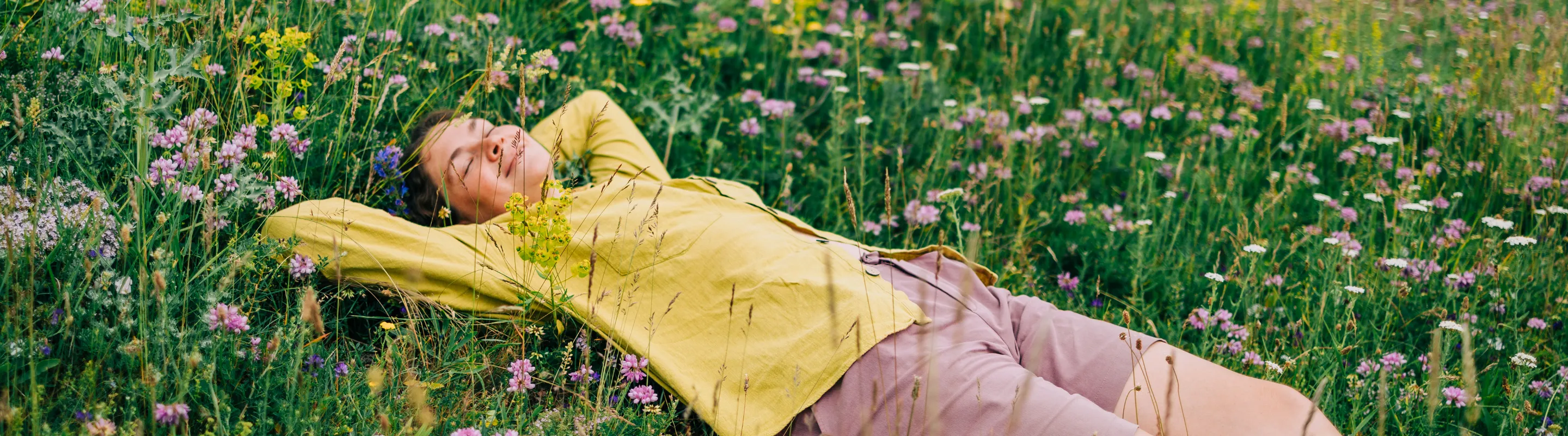 a woman with travel insurance for nature trips smiles as she rests in a wildflower field on vacation