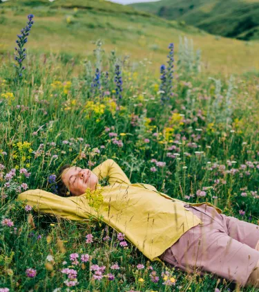 a woman with travel insurance for nature trips smiles as she rests in a wildflower field on vacation