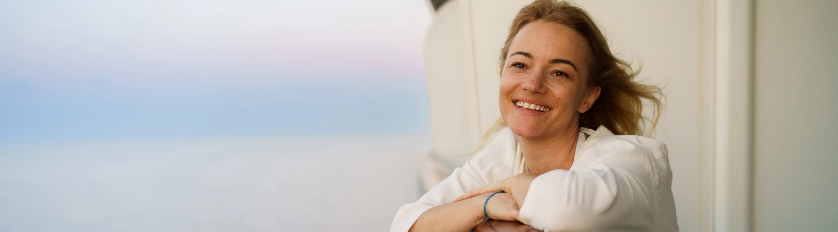 a woman with solo travel insurance smiles on a cruise ship balcony overlooking the ocean 
