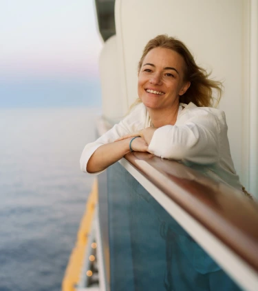 a woman with solo travel insurance smiles on a cruise ship balcony overlooking the ocean 