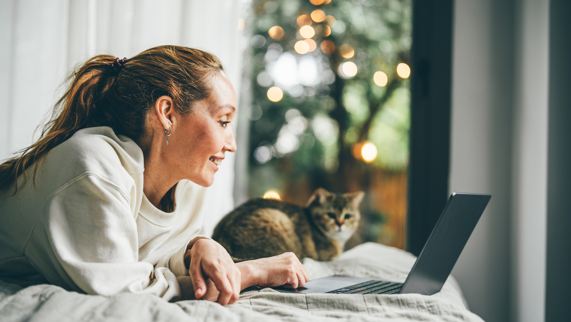 a woman uses her laptop at home with her cat, researching "How much is travel insurance?"