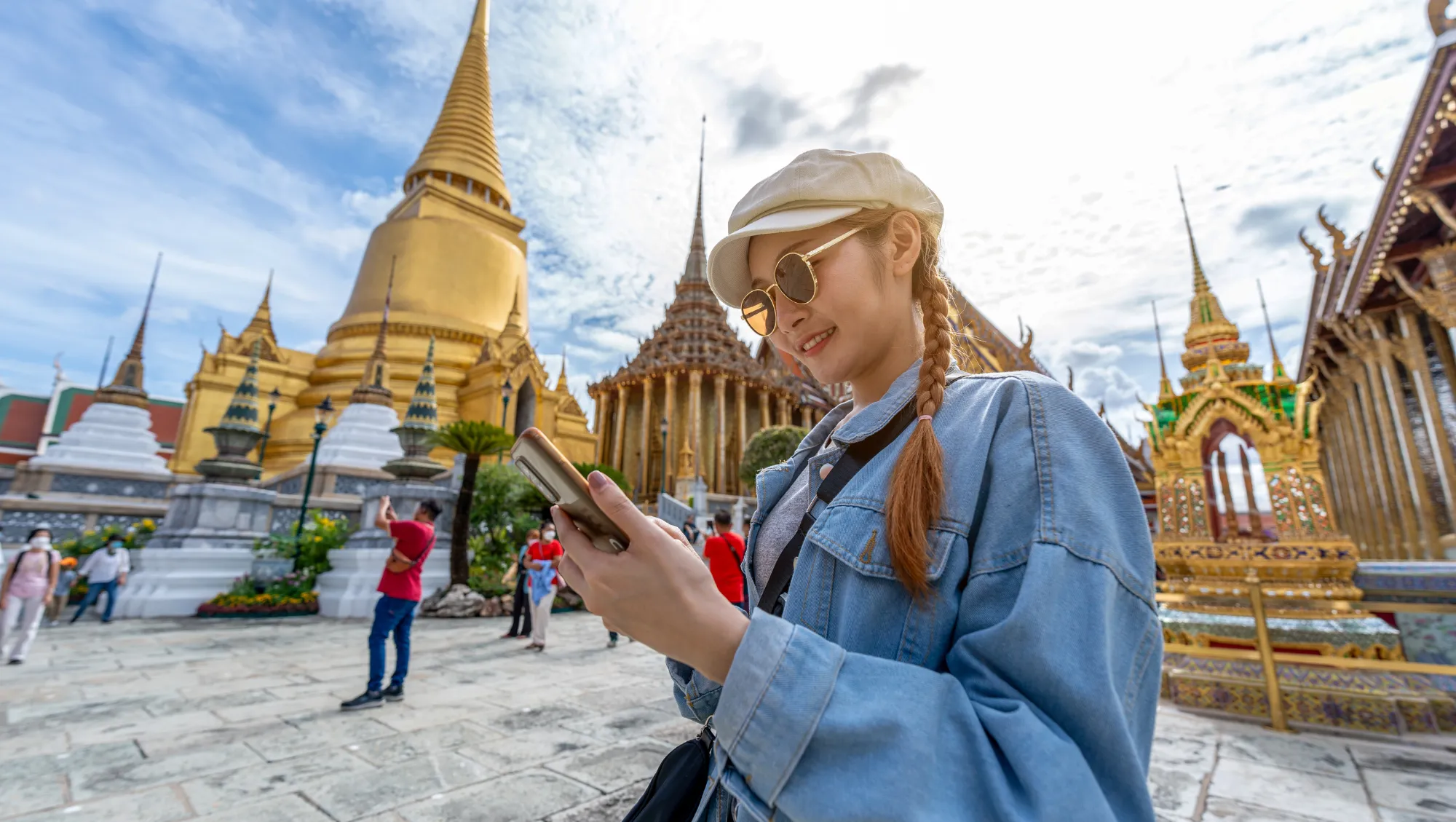 a young woman checks a travel app on her smartphone outside a Thai temple on vacation 