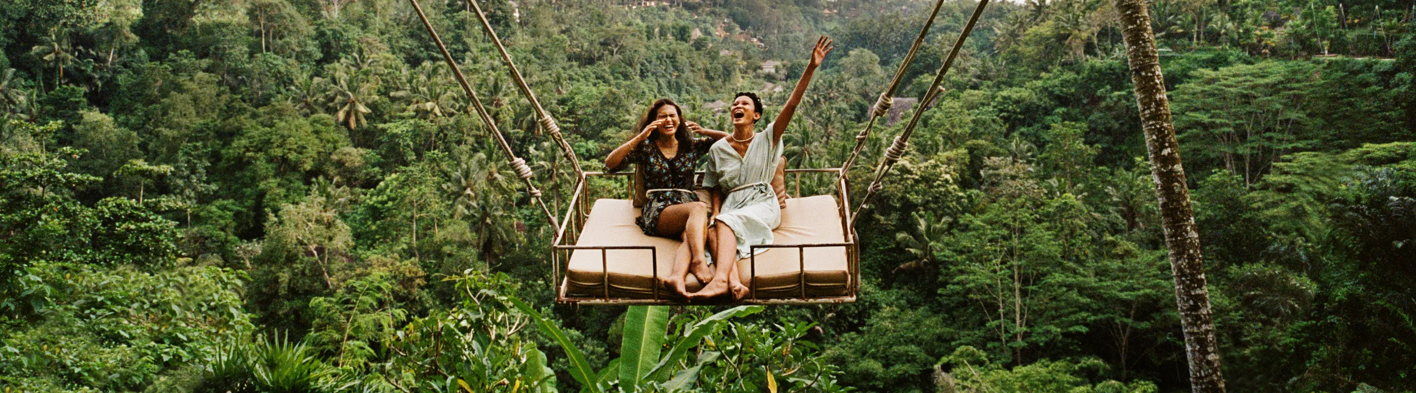 two women laugh on a giant jungle swing, insured with travel insurance for nature trips 