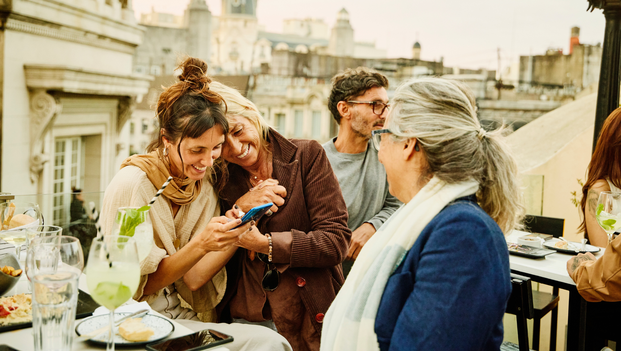 three older women dine at a rooftop restaurant on vacation and look at the travel app on their phone
