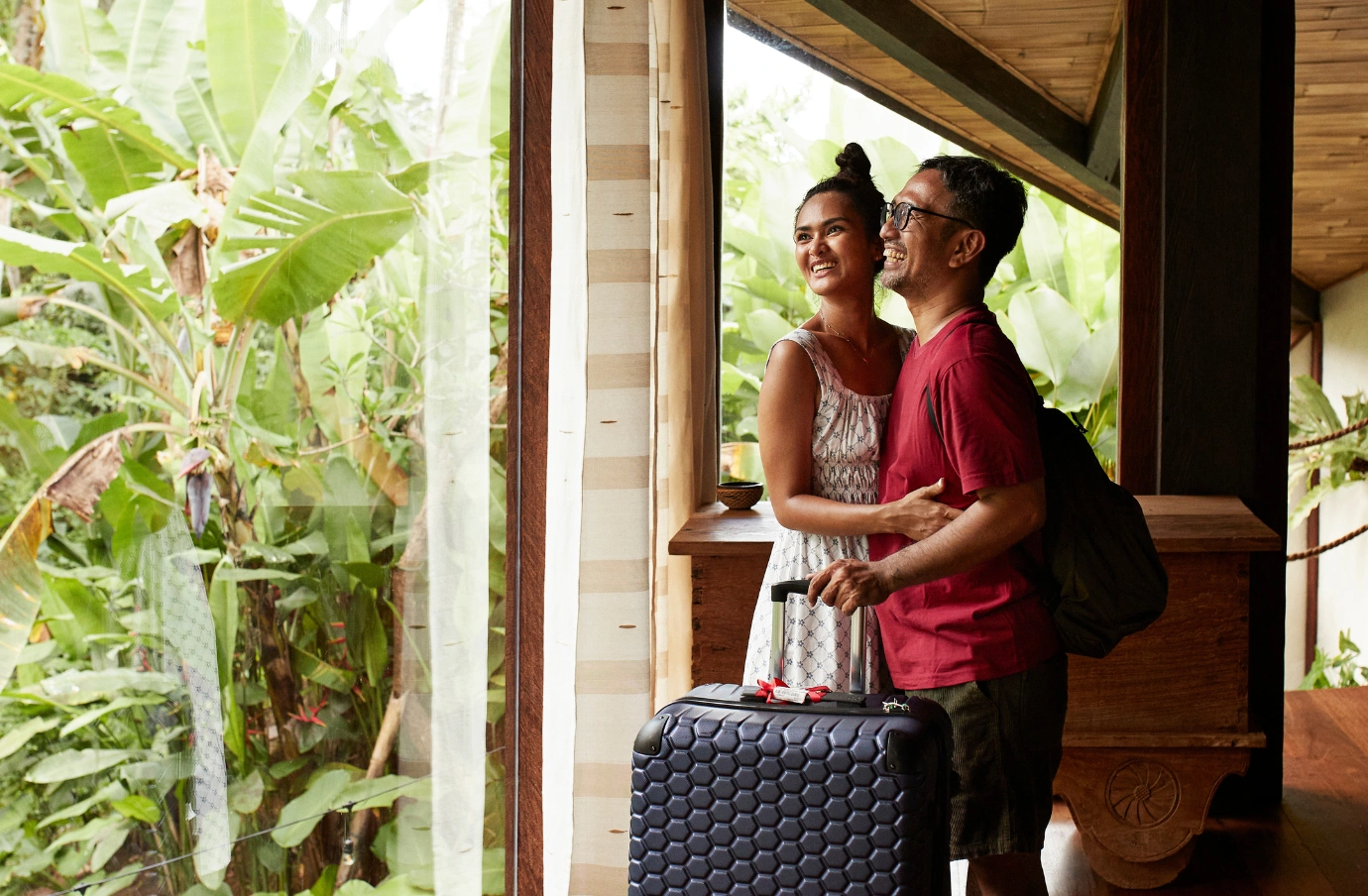 a young couple with all-inclusive travel insurance looks out the window in their jungle villa