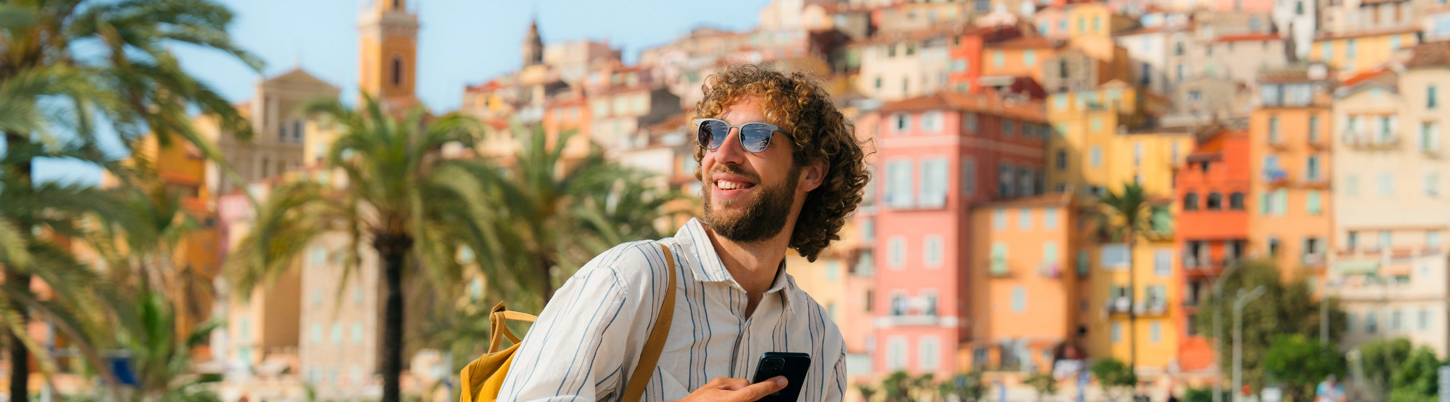 a young man with international travel insurance sits on a ledge near a colorful city in Italy on vacation