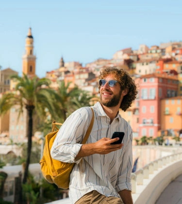 a young man with international travel insurance sits on a ledge near a colorful city in Italy on vacation
