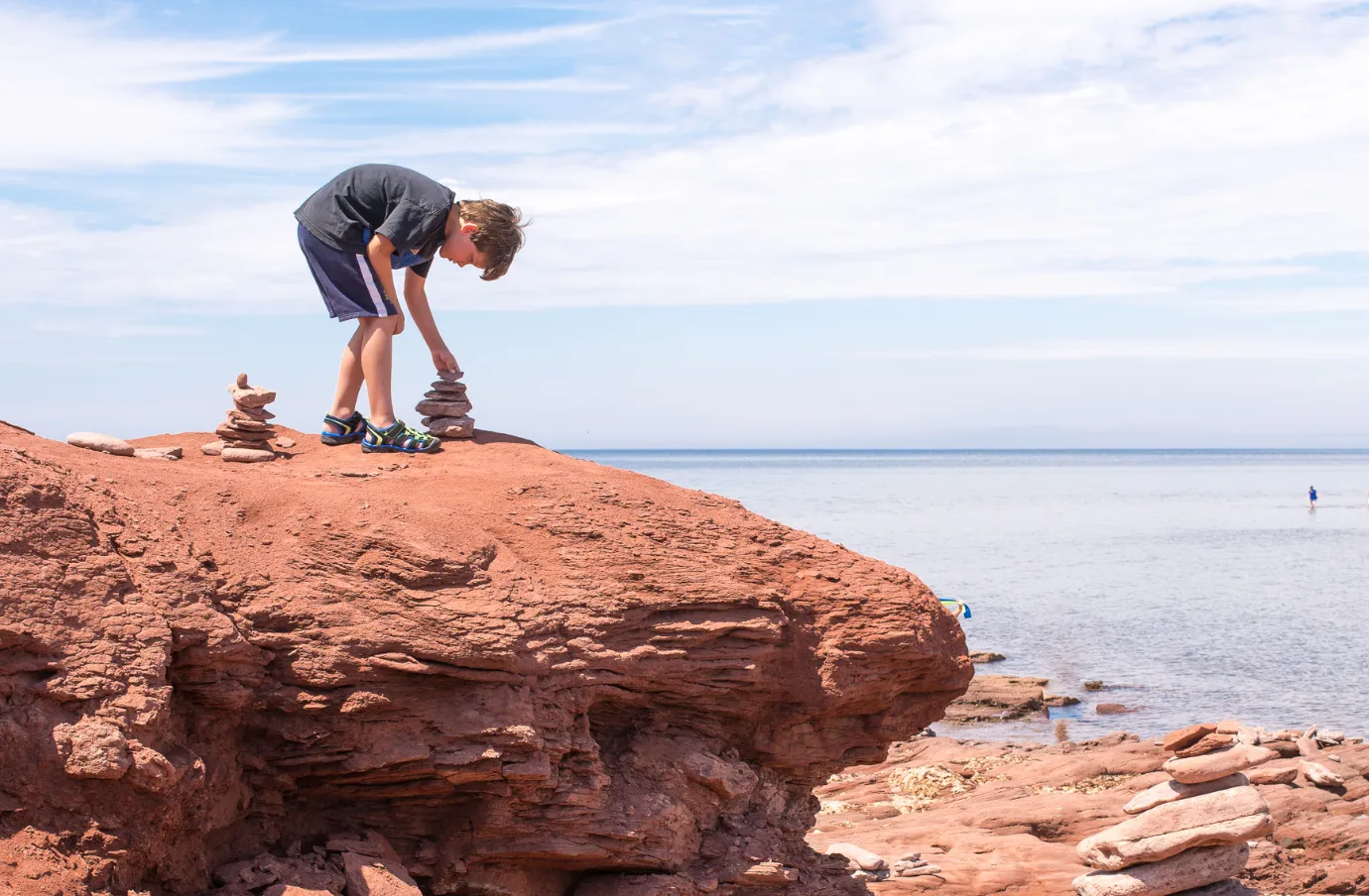 a boy builds an inuksuk on a rocky beach in PEI, insured with travel insurance for Canada