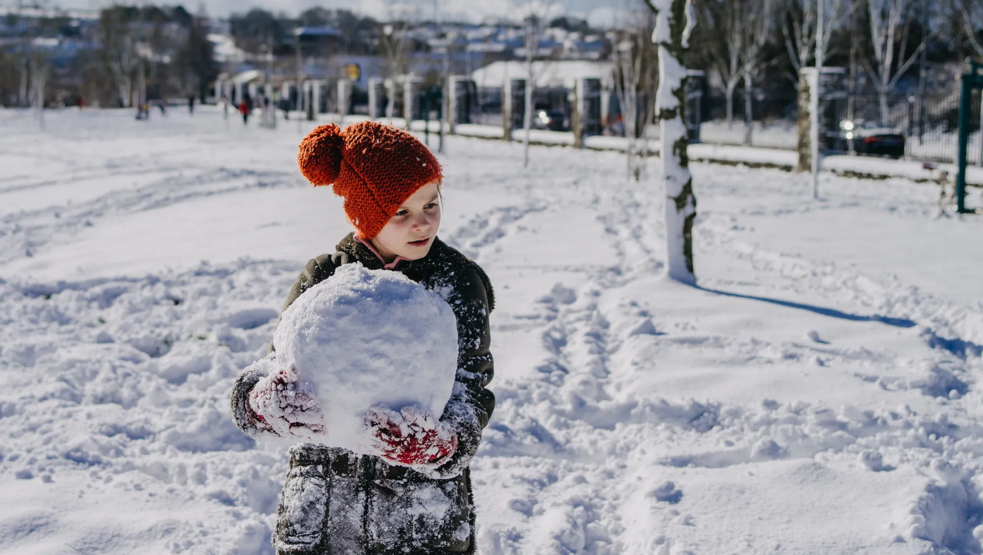 a child holds a giant snowball in Ireland on vacation after her parents researched, "Does travel insurance cover snowstorms?"