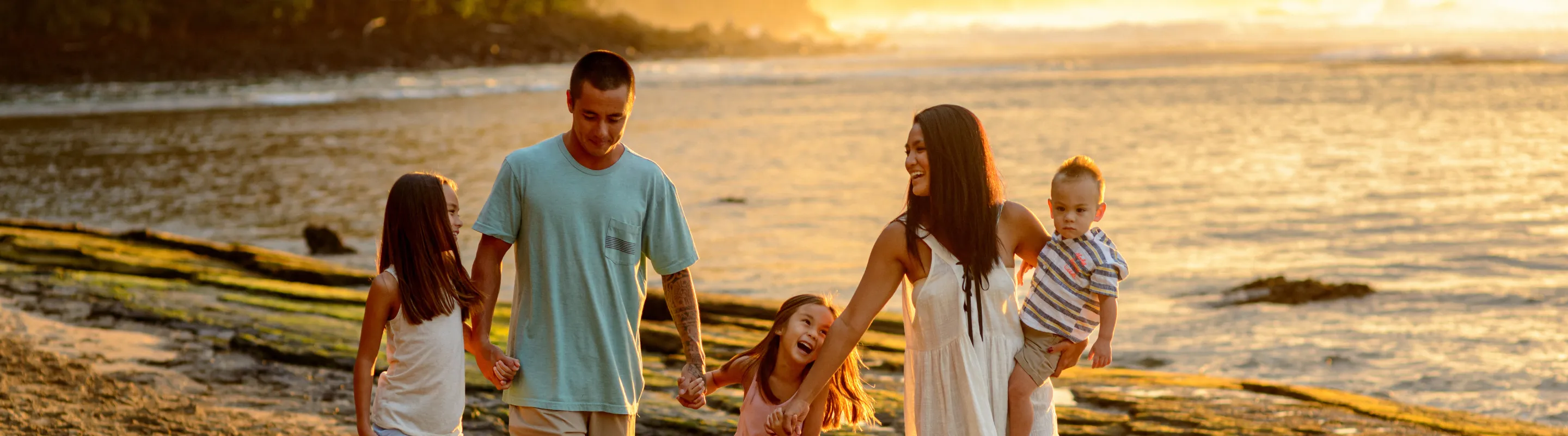 a family of five walks on the beach at sunset, insured with travel insurance for Hawaii