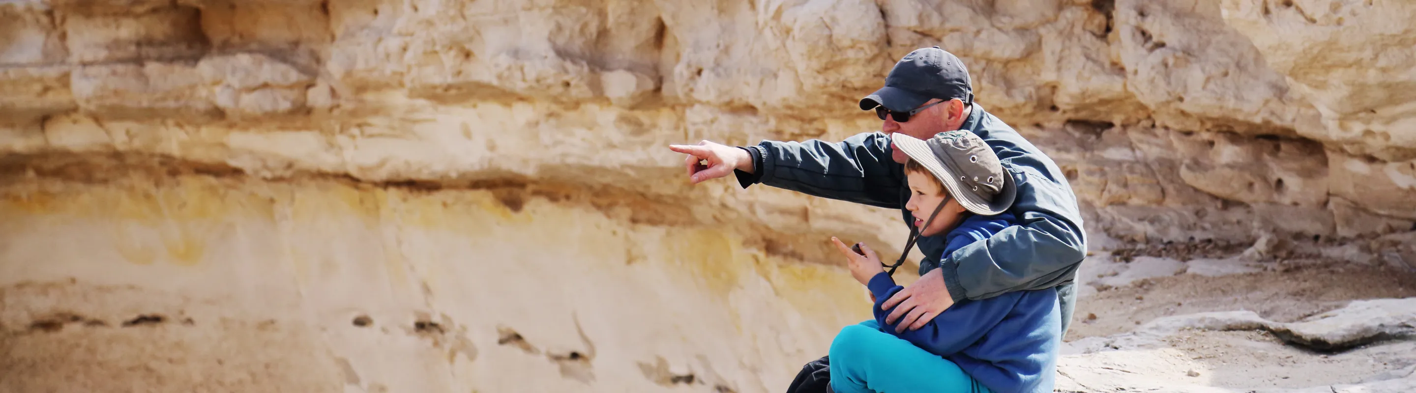 a father and boy sit down to enjoy views on a desert hike, insured with travel insurance for Israel 