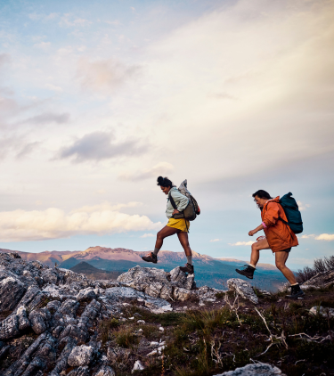 two female bushwalkers cross a rocky mountain trail, insured with travel insurance for Australia