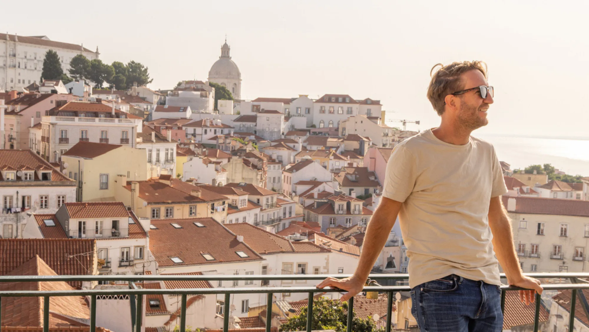 a man overlooks the city of Lisbon, Portugal, on vacation after asking "Is travel insurance worth it?"