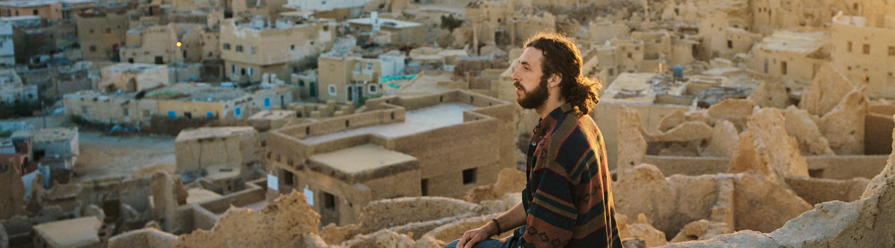 a young man sits on a ledge and overlooks the Siwa Oasis at sunset, insured with travel insurance for Egypt