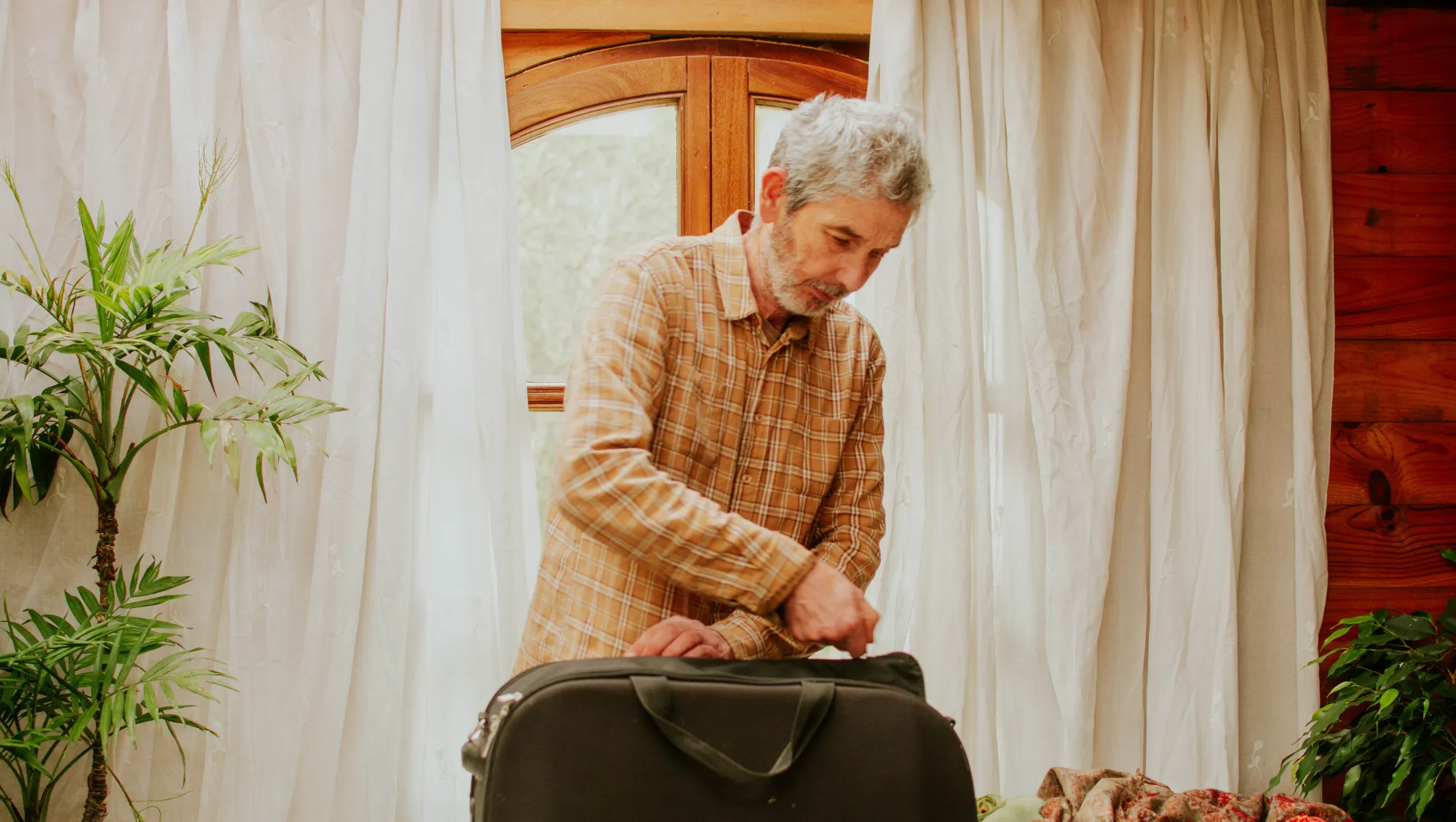 an older man zips up his suitcase for vacation, hoping to beat travel anxiety by planning ahead 